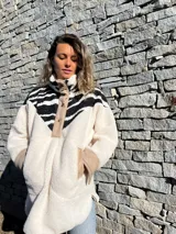 Buzo de polar color crudo con cuello alto, cierre parcial con botones a presión y mangas largas con puños de color beige. Presenta un canesú con estampado de cebra en blanco y negro.
