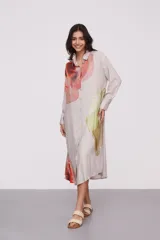 Vestido camisero midi color beige con estampado abstracto en tonos naranja, rojo, verde y amarillo. Tiene cuello camisero, mangas largas con puños abotonados y cierre frontal con botones.