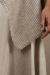 Poncho color beige con diseño a cuadros, cuello bote y terminaciones desflecadas. Tiene aberturas para los brazos en los laterales y detalles en cuero.