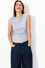 Top entallado color celeste en punto con textura. Modelo con escote bote, manga japonesa y costuras laterales fruncidas para un efecto drapeado suave.