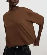 Blusa color beige, cropped y de corte amplio, confeccionada en tejido de media malla, con cuello redondo y mangas cortas.