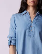 Blusa celeste en lyocell, con cuello a la base con solapa, escote en V y abertura central con botones. Manga larga regulable con presilla y botón.