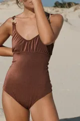 Traje de baño enterizo marrón acanalado con escote en V, breteles gruesos con argollas decorativas de resina color hueso y corte vedetina grande.