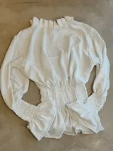 Blusa blanca de manga larga con cuello alto fruncido y detalle de smock en puños y cintura. Estampado floral en tono azul suave.