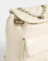 Mochila negra de cuerina acolchada con diseño de líneas diagonales. Tiene solapa con broche decorativo y botón para cerrar. Cuenta con correas regulables, manija superior de material principal y metal, y tira de ajuste de metal.