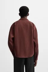 Camisa color borgoña de corte relajado, confeccionada en tejido con mezcla de viscosa. Tiene cuello solapa, manga larga con puños abotonados, bolsillo de parche en el pecho y cierre frontal con botones.