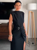 Vestido largo color crema, sin mangas, con cuello drapeado y fruncido lateral con detalle de argolla que genera una abertura frontal.