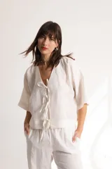 Blusa color crema confeccionada en lino, con mangas cortas, escote en V y lazos frontales.
