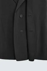 Blazer negro de corte relajado con cuello de solapa de muesca desmontable, manga larga, bolsillos frontales ocultos y cierre frontal con botones.