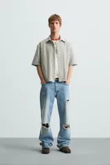 Camisa de hombre de corte boxy fit, confeccionada en tejido de algodón a cuadros en tonos beige, verde y azul. Tiene cuello solapa, manga corta y cierre frontal con botones.