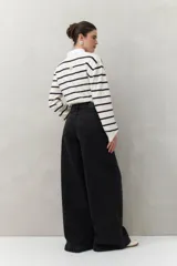 Pantalón de jean negro de calce ultra wide leg, tiro alto y silueta amplia desde la cadera hasta el bajo. Diseño clásico de cinco bolsillos y cierre con botón metálico y cremallera.
