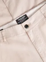 Pantalón chino de tiro medio y calce regular, color beige. Presenta cierre frontal con cremallera y botón, bolsillos laterales y bolsillos traseros de ojal. Confeccionado en tejido de sarga con mezcla de algodón, lino y elastano.