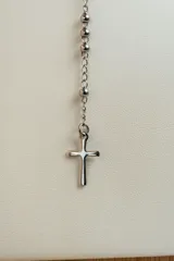 Collar tipo rosario plateado en acero quirúrgico, con cuentas y cruz colgante.