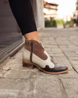 Botines de cuero marrón y blanco con diseño western, puntera redondeada y cierre lateral con cremallera. El talón tiene una tira de cuero para facilitar el calce.