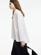 Camisa blanca de algodón con cuello camisero y botones frontales.