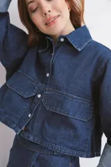 Camisa de denim azul con cuello clásico, cierre frontal con botones blancos, mangas largas con puños abotonados y dos bolsillos cargo con solapa en el pecho.