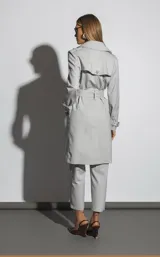 Trench gris con cuello solapa, doble botonadura, cinturón con hebilla y bolsillos laterales.