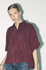 Camisa color borgoña de corte amplio, confeccionada en tejido fluido con modal. Tiene cuello solapa, manga corta con dobladillo y cierre frontal con botones.