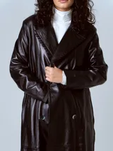 Trench largo de cuero negro con doble botonadura, solapas con muescas y costuras decorativas.