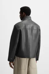Cazadora cropped de piel negra, con cuello alto, cierre frontal con cremallera, bolsillos de parche en el pecho y puños con botón.
