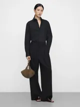 Bolso de mano tipo cóctel con diseño en forma de abanico, confeccionado con abalorios y pedrería tejidos en tricot de color gris metálico. Presenta un compartimento principal con cierre de cremallera y magnético, y un asa de mano metálica circular con logo grabado.