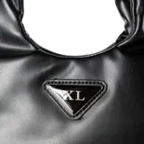 Cartera negra de cuero sintético con doble asa, una corta fija y otra larga extraíble. Tiene cierre principal con cremallera y broches magnéticos, tres compartimentos internos, un bolsillo con cremallera y otro abierto. El logo de la marca es un triángulo metálico plateado.