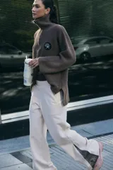 Sweater marrón de punto con cuello polo, cierre de cremallera parcial y parche bordado en el pecho.