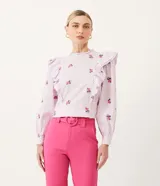 Blusa de algodón a rayas verticales blancas y lilas, con bordado de rosas rosadas. Tiene cuello redondo con volados, mangas largas y volados en los hombros.