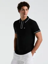 Chomba negra de piqué con cuello clásico, tapeta de dos botones y bolsillo de parche en el pecho con logo bordado. Detalles de ribete blanco en cuello y mangas.