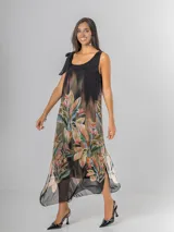 Vestido midi negro con estampado tropical de hojas y flores en tonos tierra, naranja y verde. Es de tirantes anchos con nudo regulable en el hombro y tiene aberturas laterales.