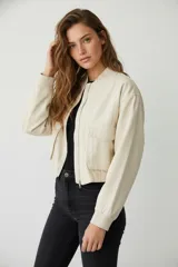 Campera corta color beige, estilo bomber, de manga larga y cierre frontal con cremallera. Tiene dos bolsillos con solapa en el pecho.
