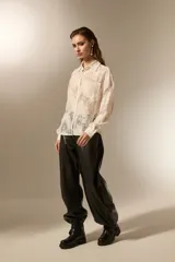 Camisa negra de poliamida con diseño calado de encaje floral, corte holgado, cuello camisero, botones frontales y mangas largas.