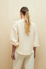 Camisa color crema a rayas verticales finas, de cuello mao, mangas 3/4 abullonadas con elástico en los puños y cierre frontal con botones de nácar.