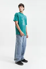 Remera verde con estampado de planta de marihuana y texto en color celeste.