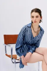 Camisa celeste con rayas verticales blancas, de corte holgado y mangas largas abullonadas con puños elásticos. Tiene cuello camisero, cierre frontal con botones y lazo en la cintura.