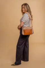 Bandolera de diseño moderno, color beige rosado, con correa regulable y bolsillo frontal con cierre.