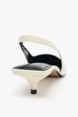 Zapato destalonado color crema con tacón fino y adorno en la parte delantera.