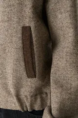 Campera estilo bomber de cuello redondo, color beige jaspeado, con cierre frontal de broches y bolsillos delanteros con ribete marrón.