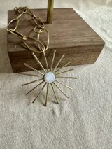 Collar con cadena de eslabones grandes color dorado y dije con forma de sol con centro de nácar blanco y rayos dorados.