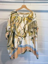 Blusa de satén con estampado de cadenas y hojas en tonos blanco, marrón y negro. Tiene corte amplio, mangas cortas y cuello redondo. Se ajusta a la cintura con un cinturón elástico negro con hebilla dorada.