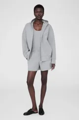 Campera gris con capucha y cierre frontal, confeccionada en tejido de buceo. Tiene corte holgado, hombros caídos, bolsillos tipo canguro y logo bordado en el pecho.