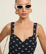 Vestido midi evasé sin mangas, confeccionado en tejido airflow con estampado de caracolas. Presenta escote corazón, breteles medianos con elásticos, recortes fruncidos en la cintura y en el bajo, y cierre lateral con cremallera invisible.