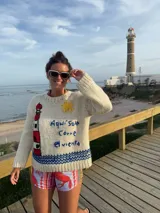 Sweater de lana color crema, tejido y bordado a mano con motivos de faro, sol y la frase "Aquí solo corre el viento".