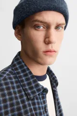 Camisa de hombre a cuadros azules y negros, de corte cuadrado, con cuello solapa, manga larga con puños abotonados, cierre frontal con botones y bolsillos de parche con solapa en el pecho.