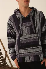Buzo estilo mexicano con capucha, de tejido grueso a rayas horizontales en tonos negro, gris y violeta. Tiene un bolsillo tipo canguro en el frente y cordones ajustables en la capucha.