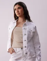Campera de jean blanca, marca Baccini, con cuello solapa, bolsillos delanteros, abertura central con botones metálicos y terminación desflecada en el ruedo.