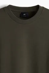 Remera de algodón pesado color verde oscuro, con cuello redondo ribeteado, hombros caídos y corte oversized.