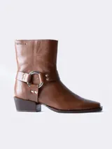 Bota corta de cuero color marrón, con puntera ligeramente afilada y detalle de correa con herraje metálico circular y tachas. Su taco bajo y ancho brinda estabilidad y comodidad.