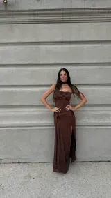 Vestido largo marrón strapless con frunce en el busto, tajo lateral y nudo decorativo en la cadera. Incluye choker al tono.