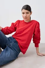 Sweatshirt rojo de manga larga con cuello redondo y calados bordados en los hombros y mangas.